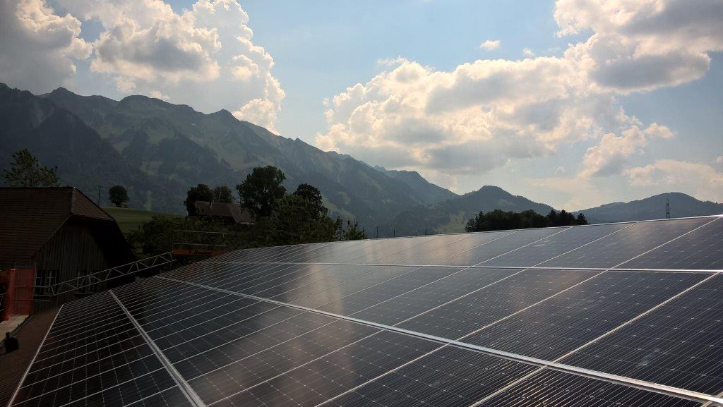 Eine große Fläche mit Solarpaneelen auf einem Dach, im Hintergrund eine Berglandschaft unter einem bewölkten Himmel.