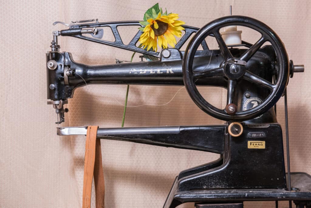 Eine alte schwarze Nähmaschine der Marke Adler, dekoriert mit einer Sonnenblume, vor einem beigen Hintergrund.