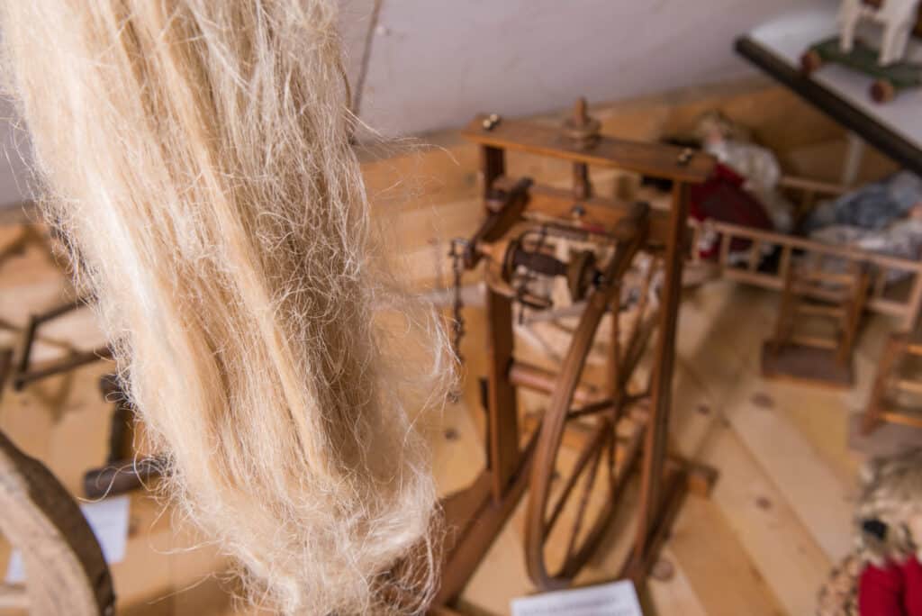 Ein historisches Spinnrad in einem Raum mit Holzfußboden, umgeben von flauschigen Fasern.