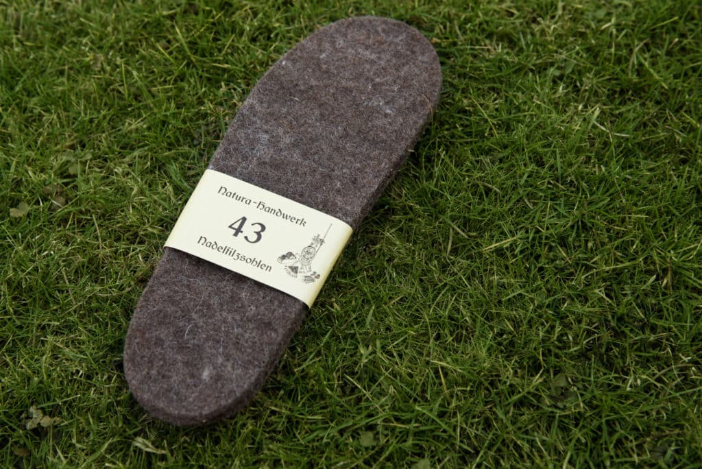 Eine Filzeinlage mit der Aufschrift "Natura-Handwerk 43 Nadelfilzsohlen" liegt auf einer Grasfläche.