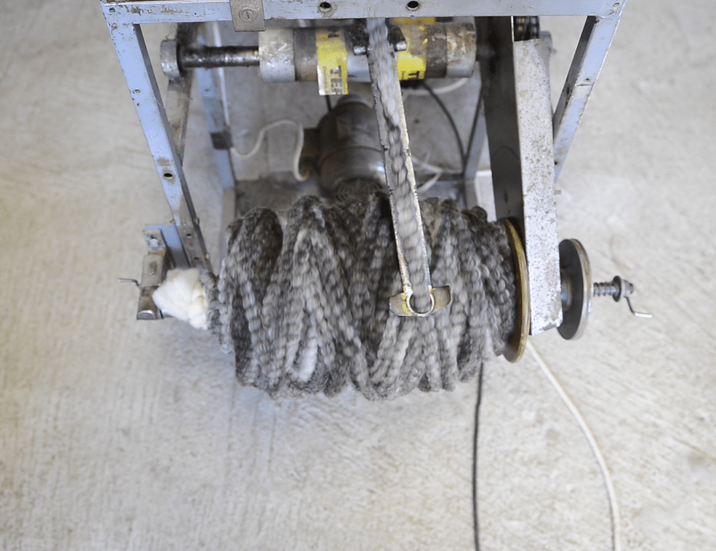 Eine alte graue Maschine mit einem großen Bündel aus grauem Seil an der Vorderseite, das zusammengedreht ist, auf einem Betonboden stehend.