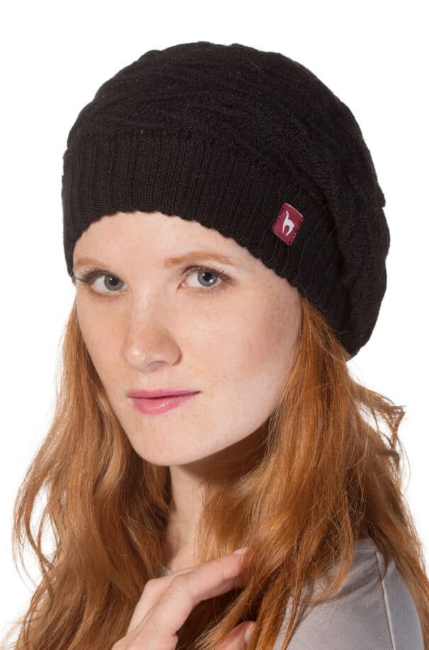 Frau mit langen roten Haaren trägt eine schwarze Strickmütze mit einem kleinen roten Logo-Label an der Seite.