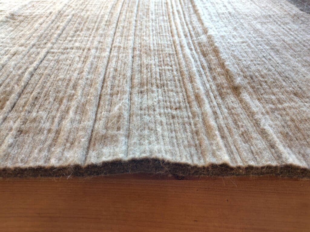 Eine strukturierte Oberfläche eines hellbraunen, dichten Filzmaterials.