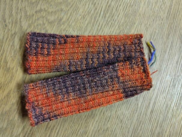 Gestrickte Armstulpen in rot-brauner Farbkombination auf einem Holztisch.