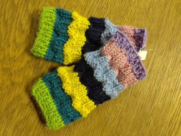 Bunte, gestreifte, gestrickte Armwärmer auf einer Holzoberfläche.