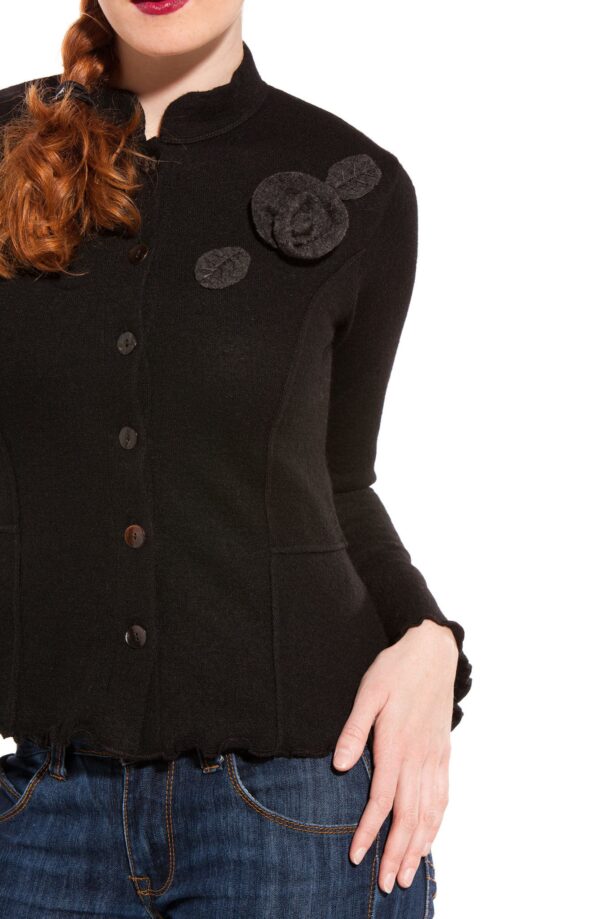 Frau trägt eine schwarze Jacke mit Knöpfen und großer Stoffblume, dazu eine blaue Jeans.