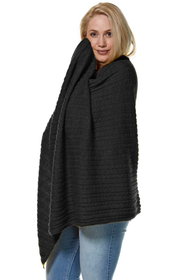 Eine Frau mit blonden Haaren, die in eine schwarze, strukturierte Decke gehüllt ist und dabei Jeans trägt.