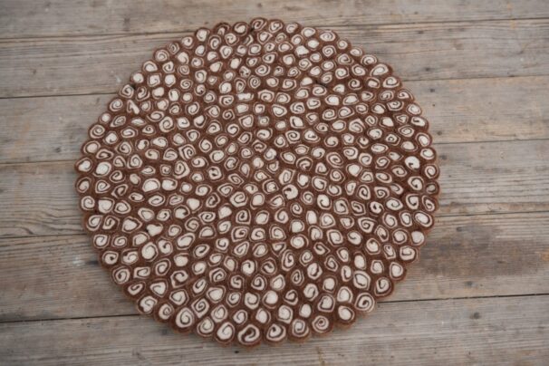 Runde Filzmatte auf Holzboden, bestehend aus kleinen, spiralförmigen braunen und weißen Mustern.