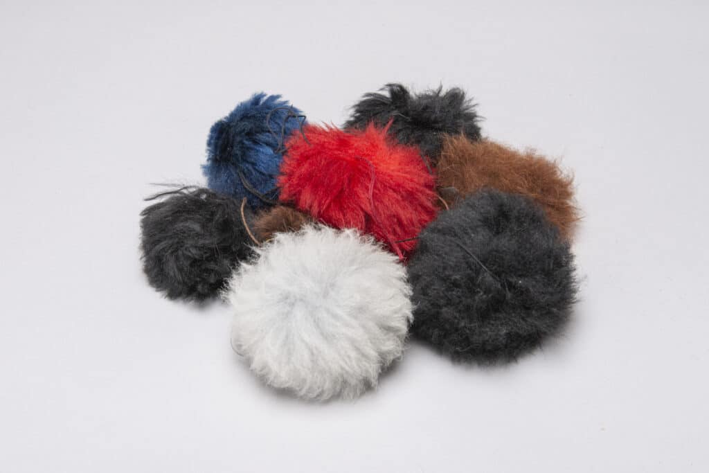 Eine Sammlung von flauschigen, bunten Pompons in den Farben Weiß, Schwarz, Blau, Rot und Braun auf weißem Hintergrund.