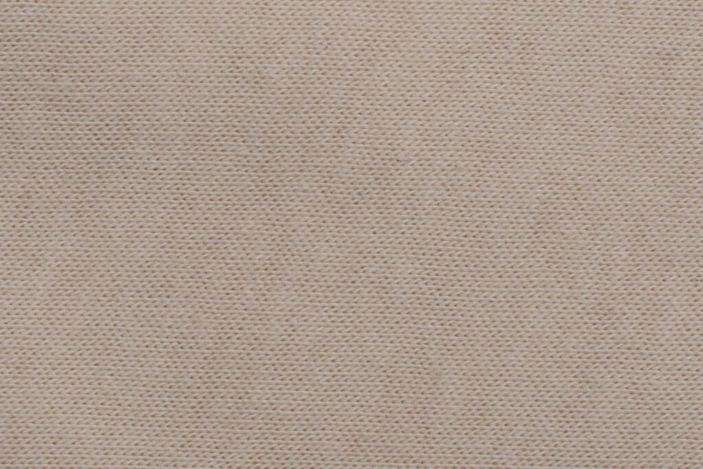 Nahaufnahme einer beige melierten Stoffstruktur mit deutlich sichtbarem Strickmuster.