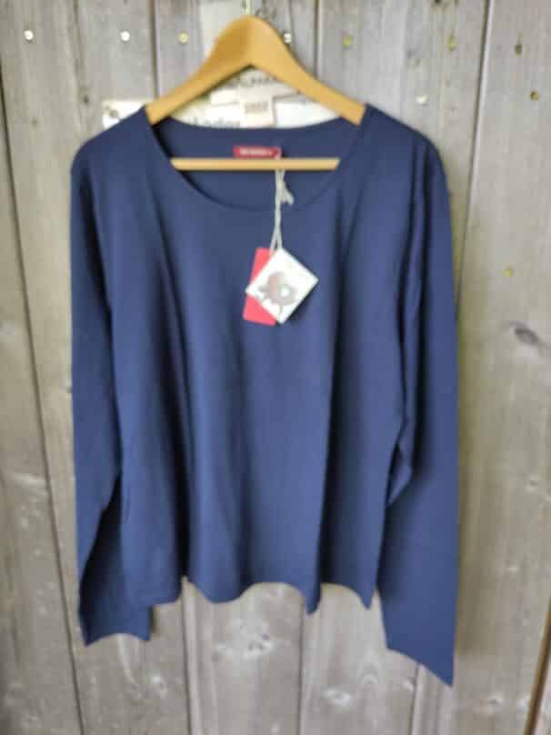 Blaues Langarmshirt auf einem Holzkleiderbügel vor einem Holzhintergrund hängend, mit einem Etikett am Kragen.