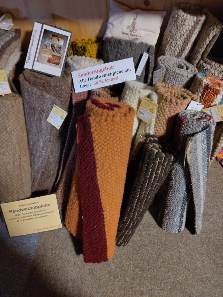 Handgewebte Teppiche in verschiedenen Farben und Mustern, mit einem Schild "Sonderangebot: Alle Handwebteppiche am Lager 50 % Rabatt".