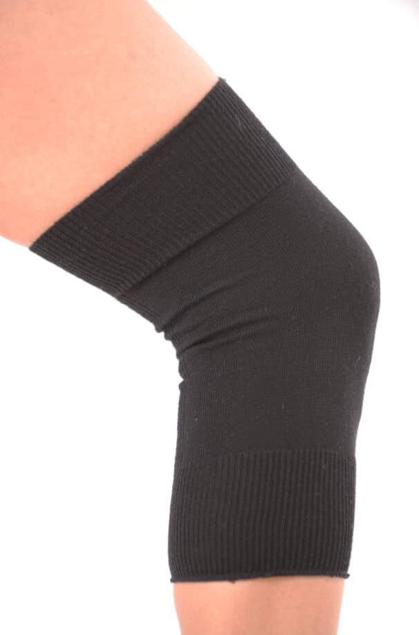 Ein schwarzer elastischer Knieschoner wird über einem menschlichen Knie getragen, vor weißem Hintergrund.