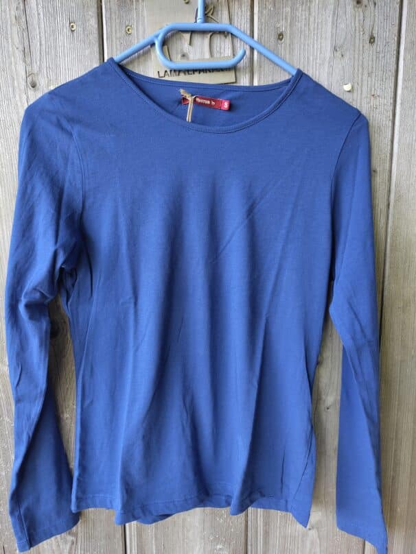 Blaues Langarmshirt auf einem Kleiderbügel an einer Holzwand hängend.