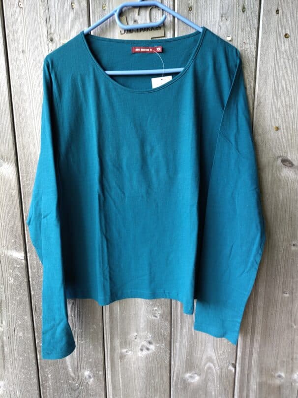 Ein türkisfarbenes Langarmshirt in Größe XXL hängt auf einem blauen Bügel vor einem Holzhintergrund.
