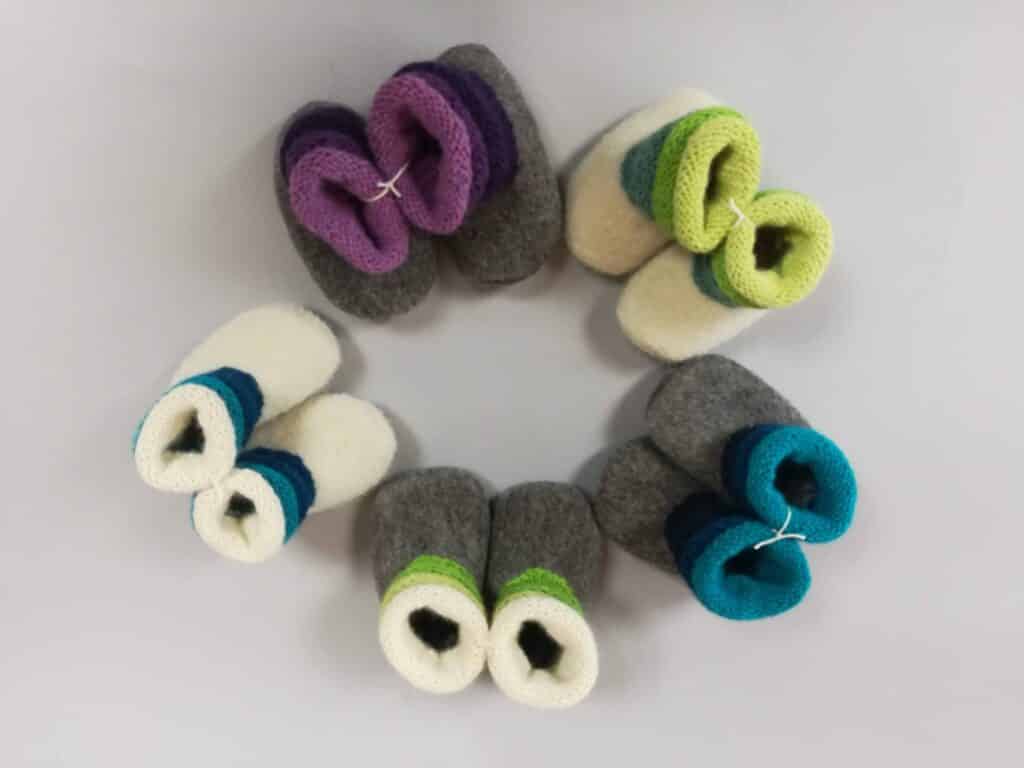 Sechs Paar gestrickte Babyschuhe in verschiedenen Farben, kreisförmig arrangiert auf einer hellen Oberfläche.