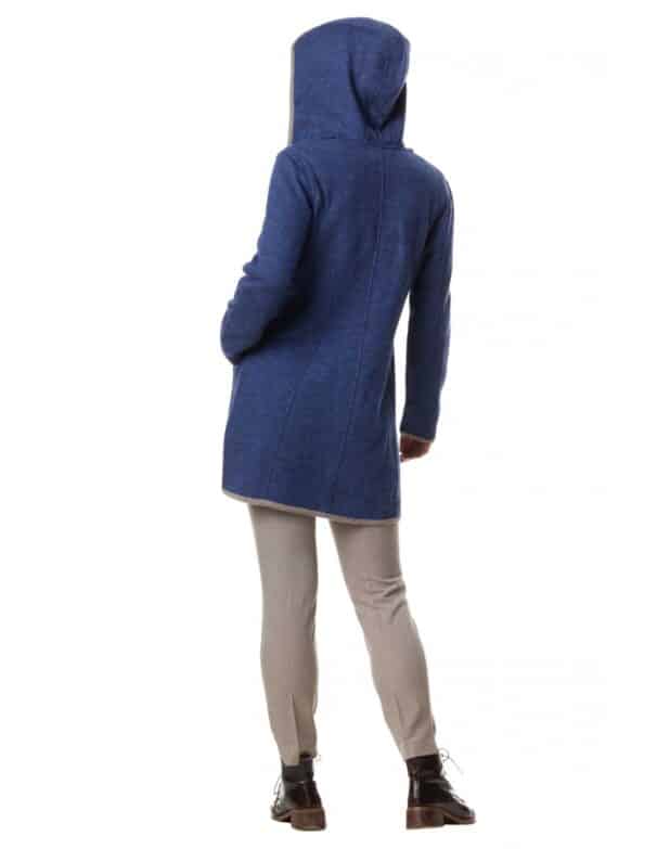 Eine Person trägt einen langen blauen Kapuzenmantel und beige Hosen, steht mit dem Rücken zur Kamera auf einem weißen Hintergrund.
