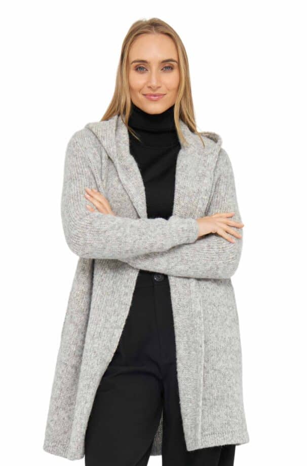 Eine Frau mit langen, offenen Haaren trägt einen grauen Strickmantel über einem schwarzen Rollkragenpullover und blickt in die Kamera.