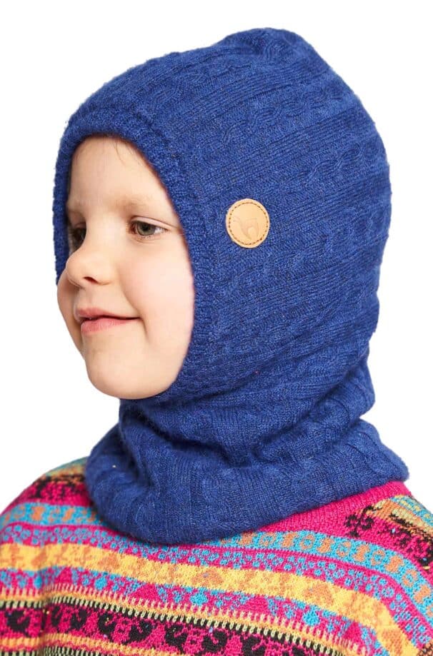 Ein Kind trägt eine blaue Strickmütze mit einem kleinen Lederlogo an der Seite und einen bunten Pullover mit verschiedenen Mustern in Gelb, Pink und Blau.