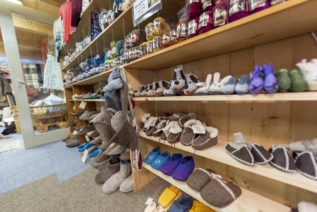 Regale in einem Geschäft mit einer Vielzahl von Filzpantoffeln, Strickartikeln und Wollknäueln, die ordentlich präsentiert sind.