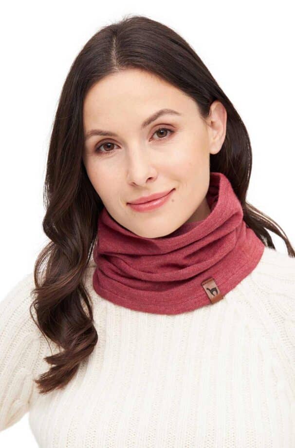 Frau mit dunkelbraunem Haar trägt einen roten Loop-Schal und einen weißen Strickpullover vor einem weißen Hintergrund.