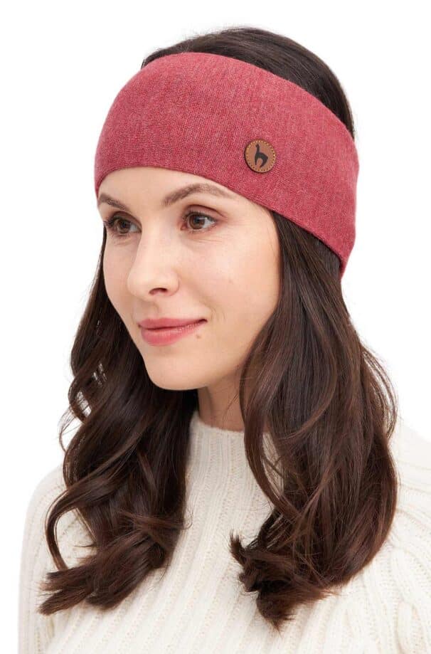 Frau trägt ein rotes Stirnband mit einem kleinen Label und einem weißen Pullover, ihre Haare sind braun und wellig.