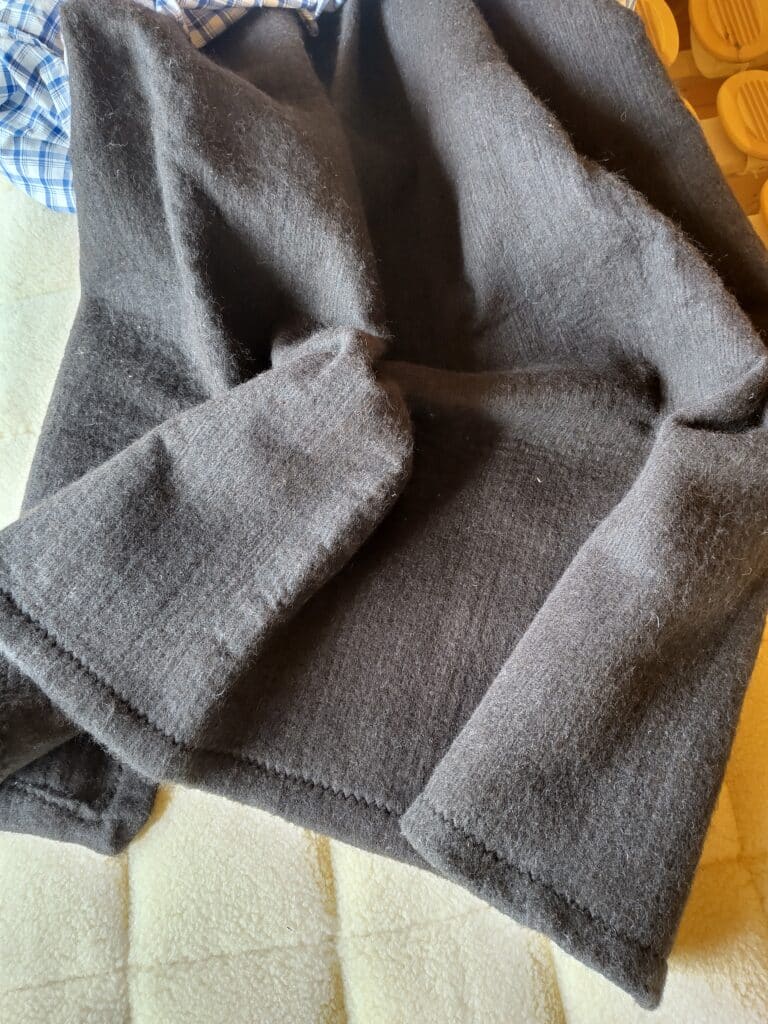 Ein grauer Stoff liegt auf einem hellen Hintergrund neben einem karierten blauen Hemd.