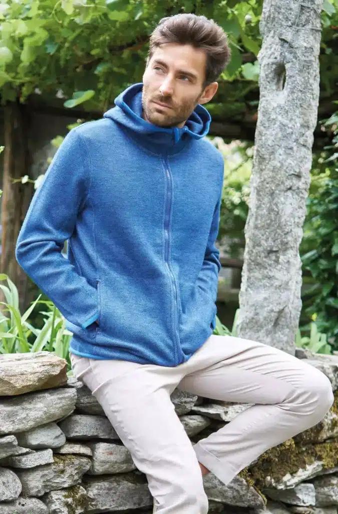 Ein Mann in einer blauen Kapuzenjacke sitzt auf einer Steinmauer im Freien.