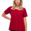 Eine Frau trägt ein rotes T-Shirt und steht mit einer Hand auf der Hüfte.