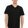 Ein Mann trägt ein schwarzes V-Ausschnitt-T-Shirt mit einem kleinen goldenen Logo auf der Brust, sowie graue Hosen, vor einem weißen Hintergrund.