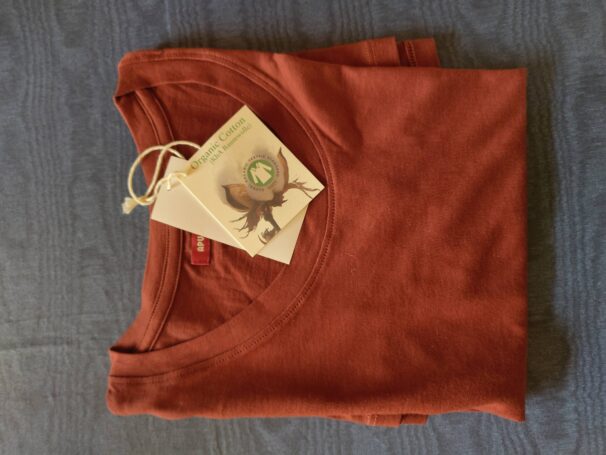Ein gefaltetes oranges T-Shirt aus Bio-Baumwolle mit Etikett auf einem dunkelblauen Hintergrund.