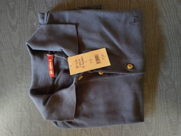 Gefaltetes dunkelblaues Poloshirt mit einem Etikett daran liegend auf einem dunklen Holztisch.