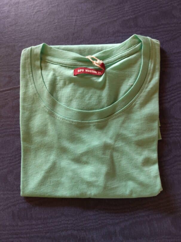 Gefaltetes grünes T-Shirt mit rotem Etikett auf dunklem Hintergrund.