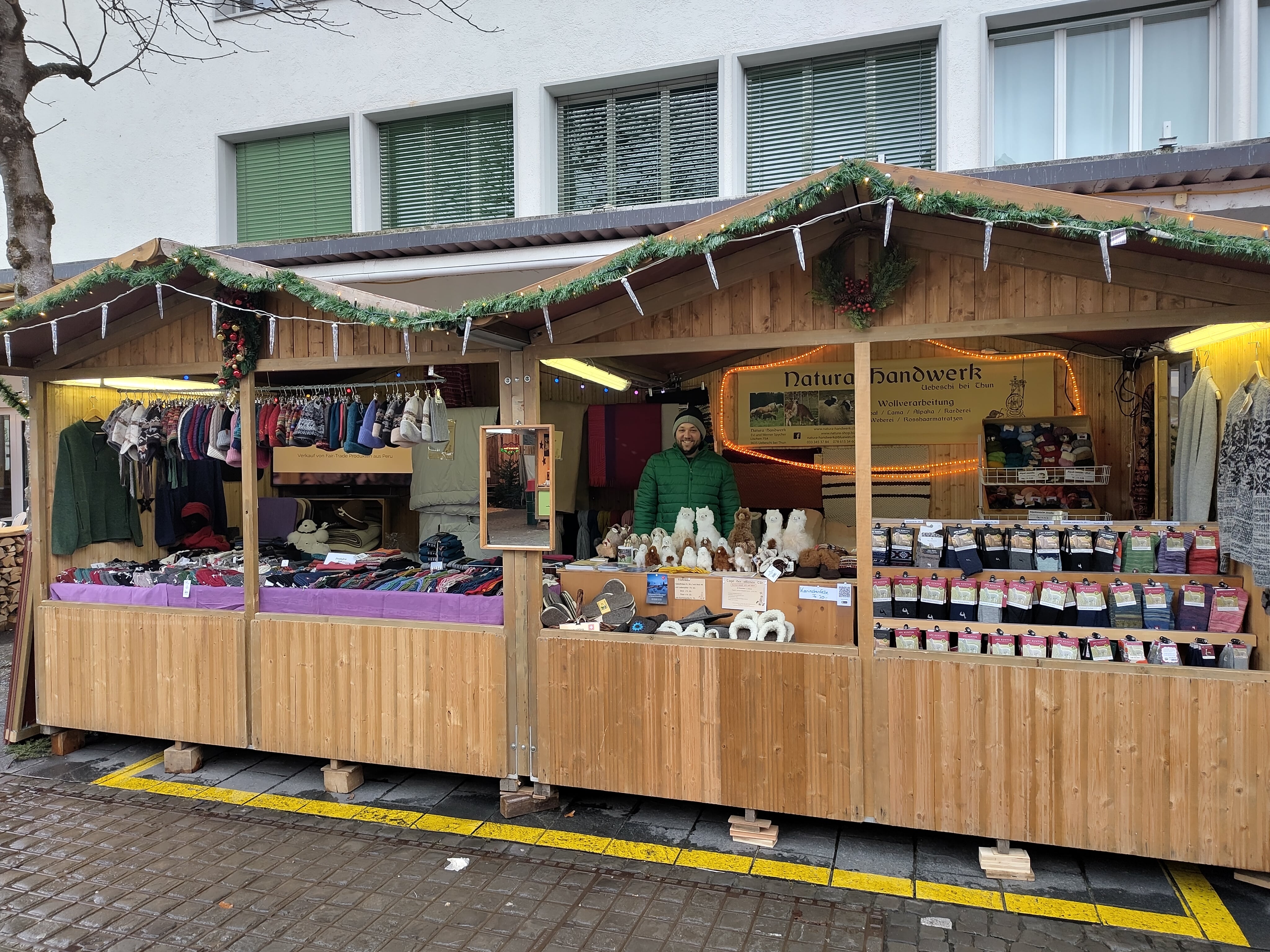 Ein Marktstand mit Kleidung, Handwerksprodukten und einem Verkäufer in einem grünen Mantel auf einem Weihnachtsmarkt.