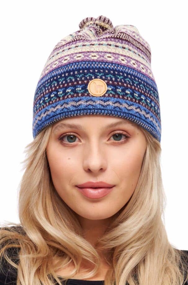 Eine Frau mit blonden, offenen Haaren trägt eine mehrfarbige Strickmütze mit einem Lederlogo auf der Stirn.