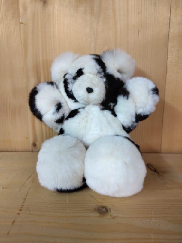 Ein schwarz-weißer Plüsch-Panda sitzt auf einem Holztisch vor einer Holzwand.