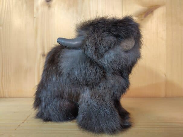 Plüschfigur eines Moschusochsen mit braunem Fell und einem Horn, vor einem Holzhintergrund platziert.