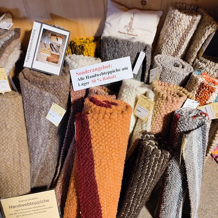 Verschiedene gerollte Handwebteppiche in verschiedenen Farben und Mustern auf einem Holzfußboden, mit einem Schild, das auf einen Rabatt von 50 % hinweist.
