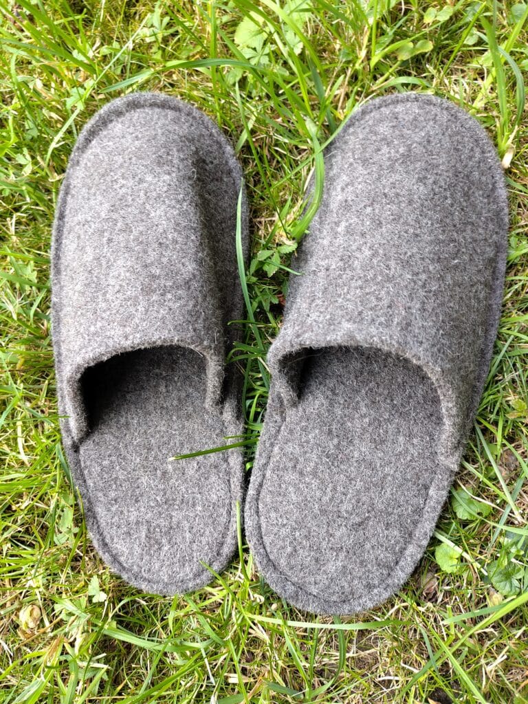 Ein Paar graue Filzpantoffeln liegt nebeneinander auf grünem Gras.