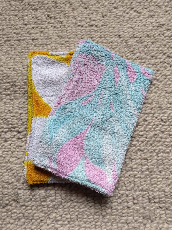 Zwei bunte, gefaltete Handtücher auf einem beigen Teppich.
