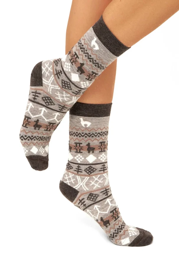 Beine, die gestrickte Socken mit geometrischen Mustern in Braun- und Grautönen tragen, auf weißem Hintergrund.