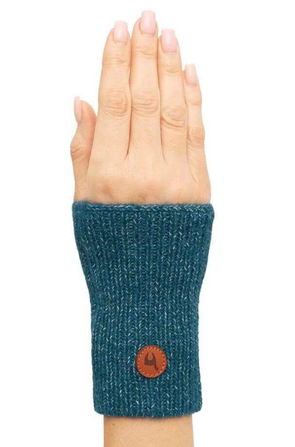 Ein Handgelenkwärmer aus blauer Strickwolle, getragen an der linken Hand, mit einem runden, braunen Lederlogo am Bündchen.