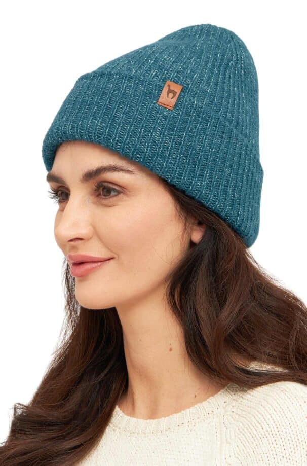 Frau trägt eine blau gestrickte Mütze mit einem kleinen, braunen Lederetikett an der Seite, dazu ein cremefarbenes Strickoberteil.