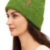 Frau trägt eine grüne Strickmütze mit einem kleinen braunen Logo auf der Seite, dazu einen cremefarbenen Pullover.