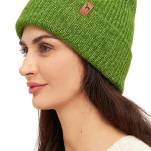 Frau trägt eine grüne Strickmütze mit einem kleinen braunen Logo auf der Seite, dazu einen cremefarbenen Pullover.