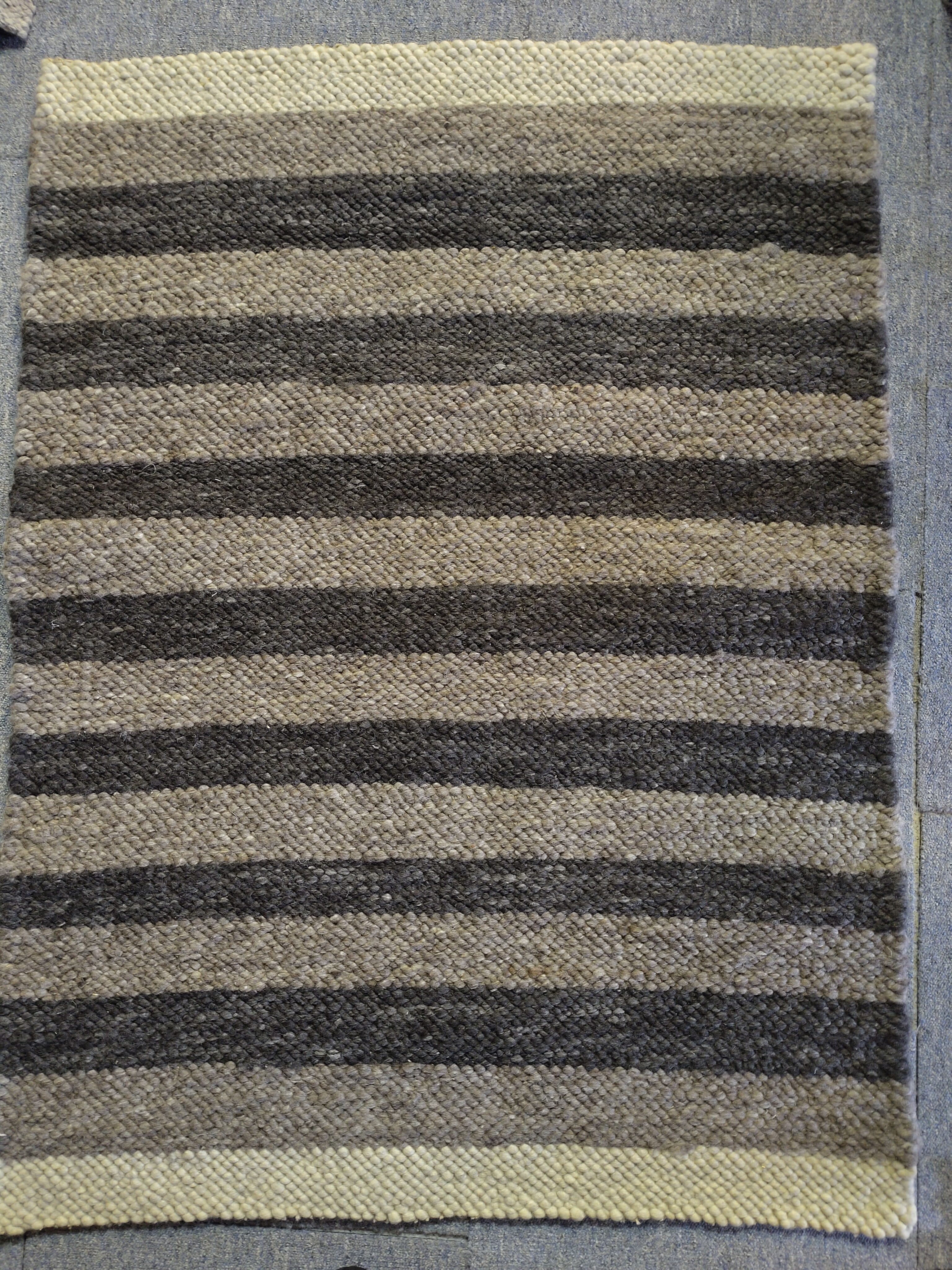 Gewebter Teppich mit abwechselnden hellen und dunklen Streifen.