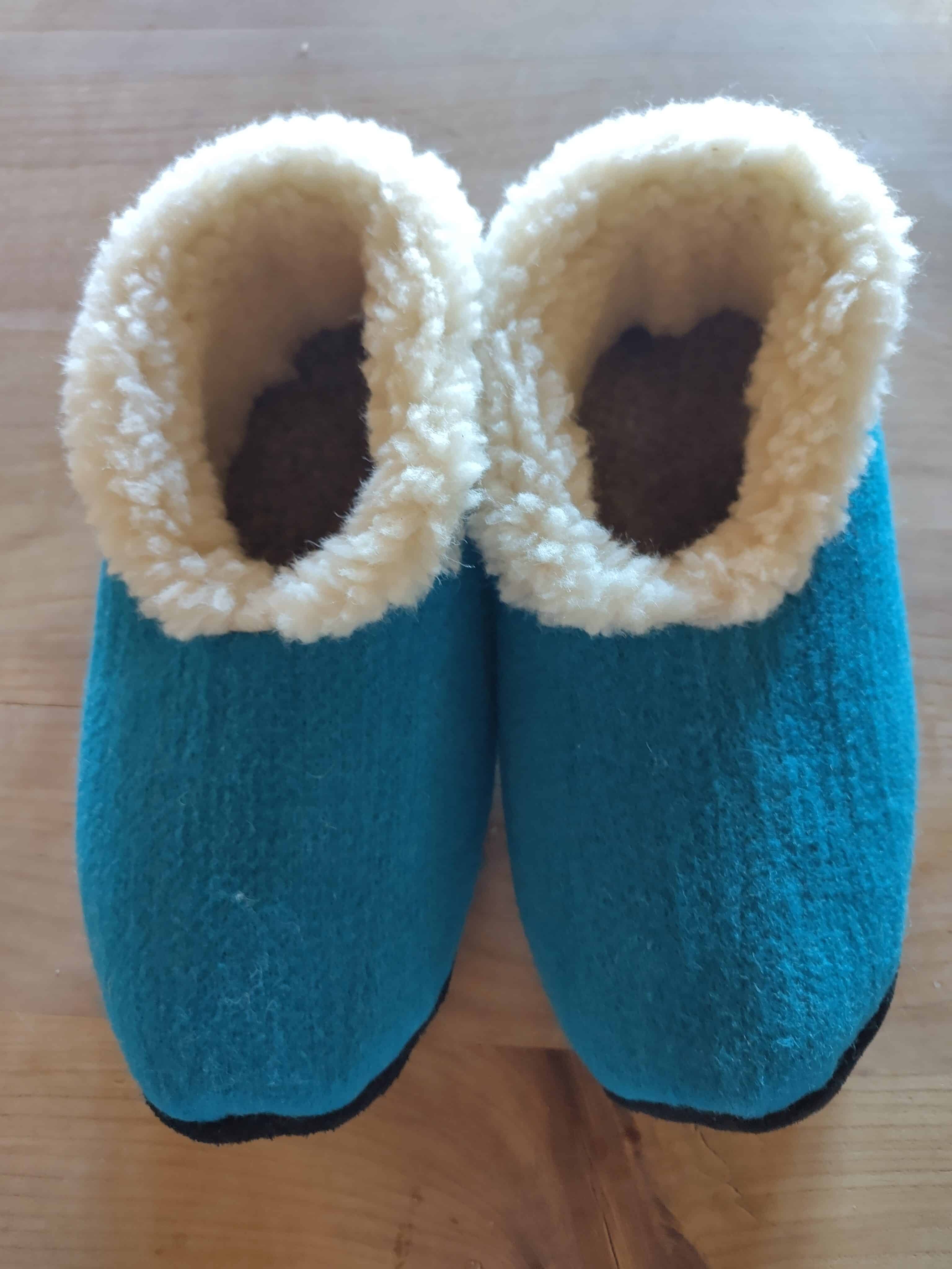 Zwei blaue Filz-Hausschuhe mit weißem, flauschigem Innenfutter auf einem Holztisch.