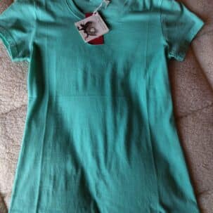 Grünes T-Shirt liegt flach auf einem beigen Stoff, mit Etikett am Kragen.