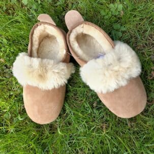 Ein Paar braune Hausschuhe mit flauschigem weißen Fellbesatz liegt auf grünem Gras.
