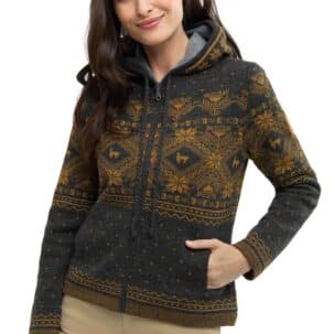 Eine lächelnde Frau trägt eine gemusterte Kapuzenjacke in Dunkelgrau und Gelb mit Reißverschluss, die Hände in den Taschen.